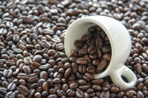 Close-up of a white cup tipped over with roasted coffee beans spilling out.